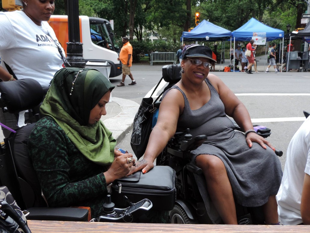 Israt Noor paints a woman's hand at Disability Pride NYC.