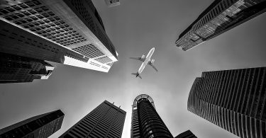 Black and white image looking between skyscrapers at an airplane overhead.