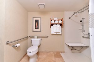 Wheelchair accessible hotel room bathroom, has a roll-in shower and peach tile floor.