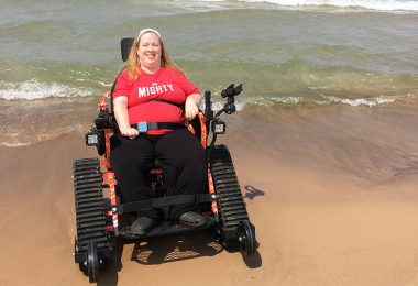 Karin Willison riding in a tank wheelchair on the beach.