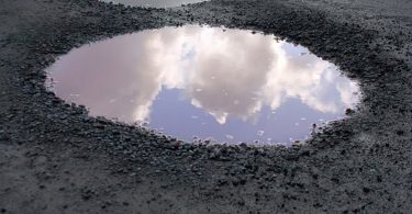 Pothole filled with water, reflecting a blue sky.